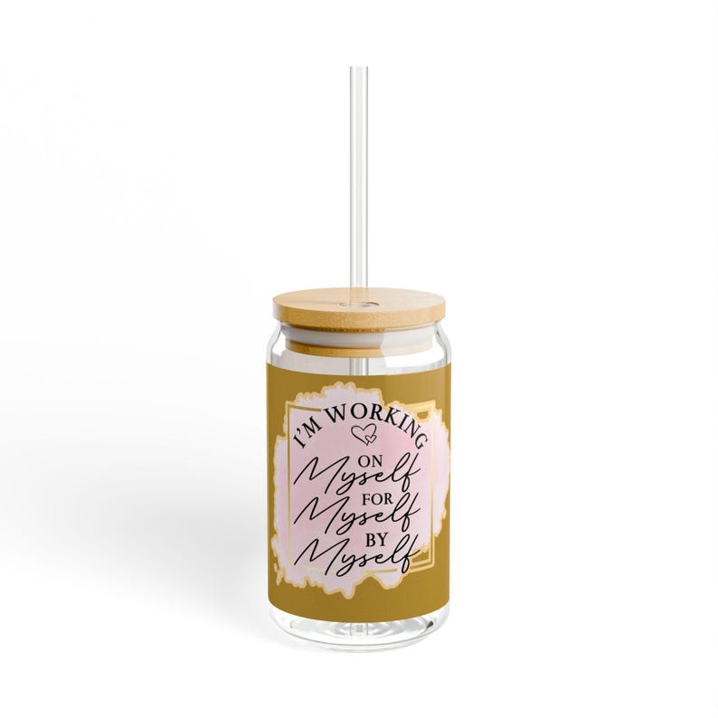 May include: A gold glass tumbler with a bamboo lid and a clear straw. The tumbler has a pink and gold design with the text "I'm working on myself for myself by myself".