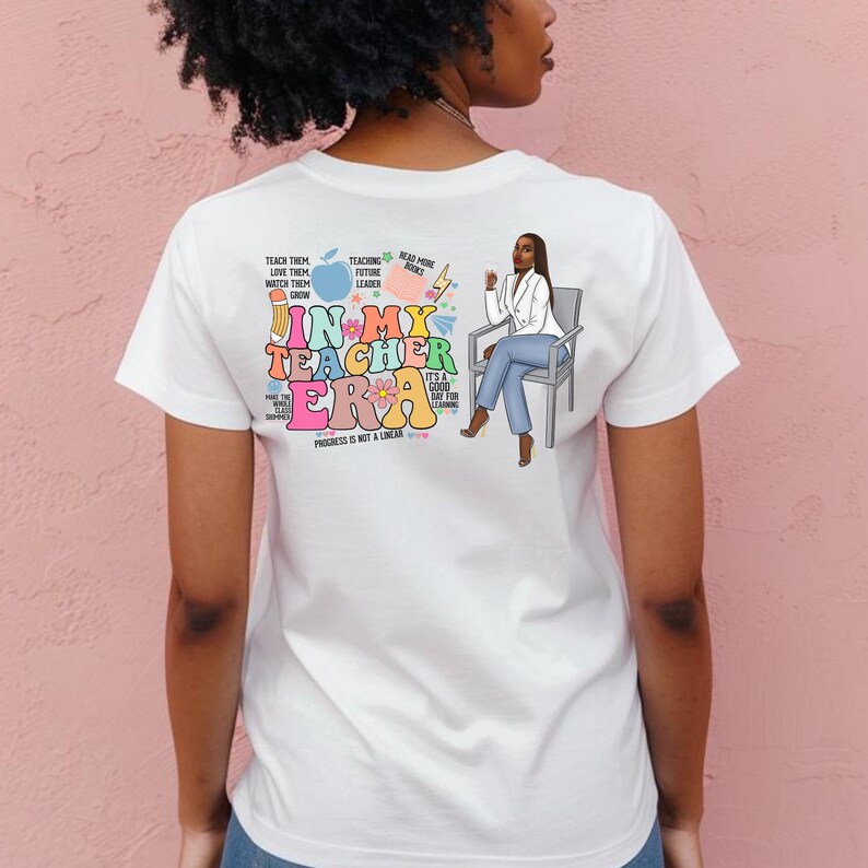 Pu&ograve; includere: Maglietta bianca con un design grafico colorato che presenta una donna seduta su una sedia. La grafica include il testo "In My Teacher Era" con uno schema di colori arcobaleno e altro testo che include "Teaching Future Leaders", "Read More Books" e "Progress is not a Linear".