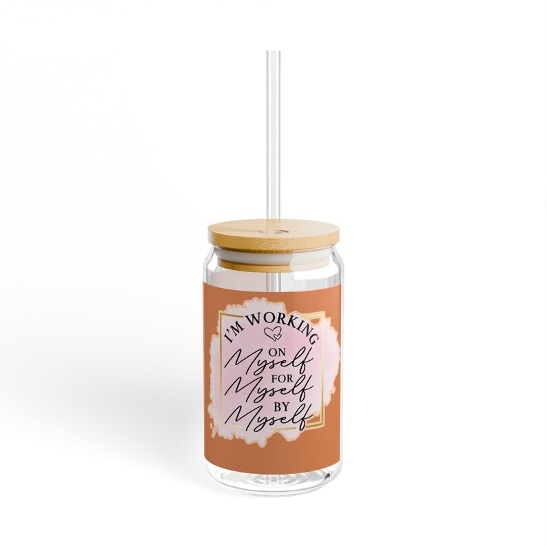May include: A clear glass tumbler with a bamboo lid and straw. The tumbler has a pink and orange watercolor design with the text "I'm Working On Myself For Myself By Myself" in black.