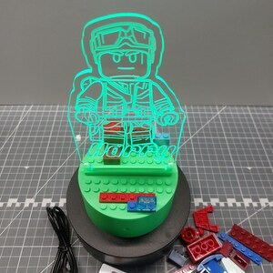 May include: A green LED night light in the shape of a Lego figure, with the name "Harry" etched into the acrylic. The light sits on a green base with Lego bricks and includes a remote control and USB cable.