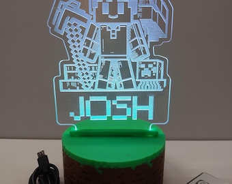 May include: A Minecraft-themed LED lamp with a pixelated character holding a pickaxe. The lamp has a green base and the name "JOSH" is illuminated. A remote control and USB cable are also visible.