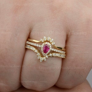 Könnte beinhalten: Ein dreiteiliger Ring-Set mit einem birnenförmigen rosafarbenen Edelstein, der von kleineren klaren Edelsteinen umgeben ist. Der Ring ist in Gelbgold gefasst.