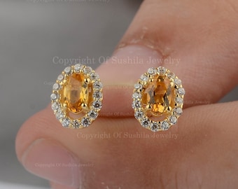 May include: A pair of gold earrings with a round halo of small diamonds surrounding a center oval topaz gemstone.