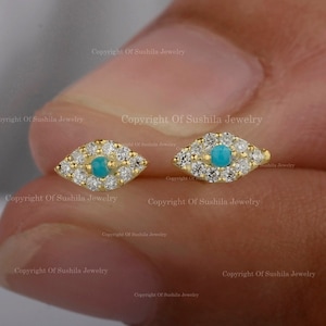 May include: A pair of gold earrings featuring a turquoise evil eye design. Each earring is set with small diamonds around the turquoise stone.