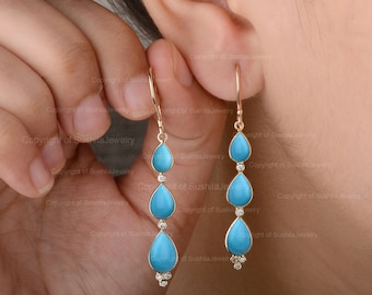 May include: A pair of gold dangle earrings with three teardrop-shaped turquoise stones and small clear diamonds on each earring.