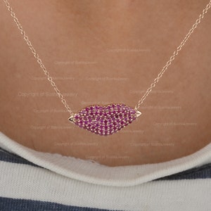 May include: A gold chain necklace with a ruby red lip pendant. The pendant is made of small ruby red stones set in gold.
