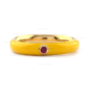 Op de afbeelding: Een gele emaille ring met een enkele rode edelsteen in het midden.
