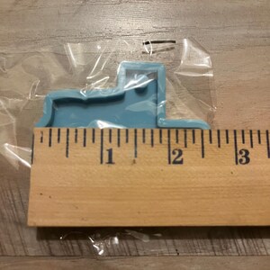 May include: A light blue silicone mould shaped like a truck. The mould is approximately 2.5 cm wide and 5 cm long. The mould is sitting on a wooden ruler.
