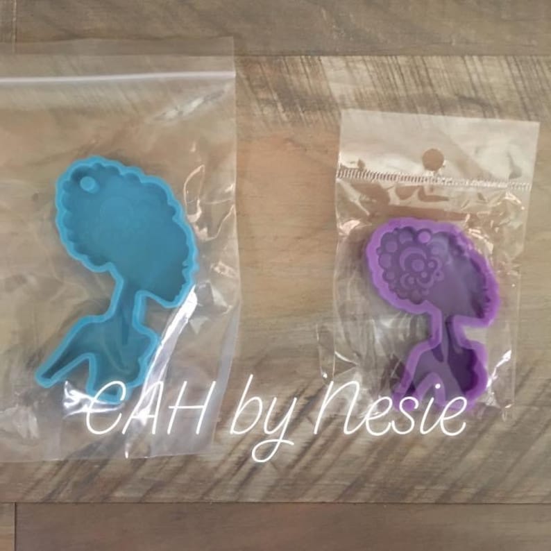 Peut inclure: Deux moules en silicone pour l'artisanat de la r&eacute;sine. Le moule de gauche est bleu clair et en forme de femme avec des cheveux cr&eacute;pus. Le moule de droite est violet et en forme de femme avec des cheveux cr&eacute;pus d&eacute;taill&eacute;s.