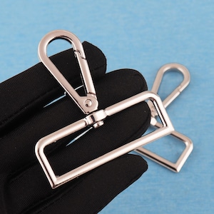 May include: Two silver-toned metal swivel lobster claw clasps with a rectangular base loop. Each clasp features a spring-loaded gate mechanism that opens inwards, attached to a rectangular frame designed for strap attachment and secure fastening.