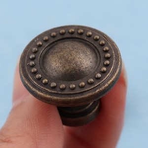 Peut inclure: Un bouton de porte rond en laiton antique avec un motif circulaire surélevé et une surface texturée.
