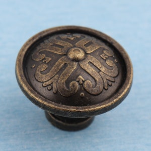 May include: A round, ornate cabinet knob with a bronze finish and a decorative floral design.