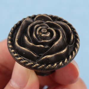 May include: A dark brown metal rose-shaped cabinet knob with a rope-like border.