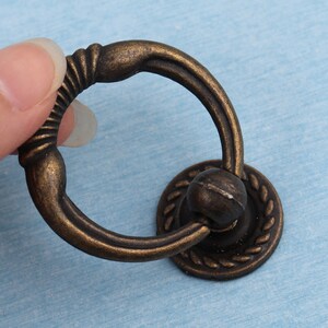 Könnte beinhalten: Antiker bronzener Ringzug-Schrank-Türgriff mit dekorativem Seil-Design.