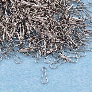 Könnte beinhalten: Ein großer Haufen silberner Schlüsselringe oder Schlüsselanhänger-Schlaufen aus Metall. Die Schlüsselringe sind auf einer hellblauen Oberfläche verstreut.