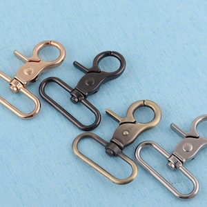 May include: Four metal swivel clasps in different finishes: gold, black, antique brass, and silver. These clasps are commonly used for attaching straps, chains, or other accessories to bags, purses, or other items.