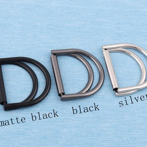 May include: Three metal D-rings in different finishes: matte black, black, and silver. Each ring has a double loop design.