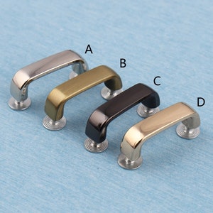 Può includere: Quattro passanti per cintura a forma di D in metallo in diverse finiture: argento, oro, nero e oro. I passanti sono disposti in fila da sinistra a destra, con il passante argentato a sinistra e il passante dorato a destra.