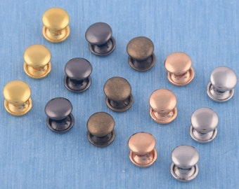 Puede incluir: Surtido de 14 botones a presión de metal en varios colores, incluyendo oro, plata, negro, bronce y oro rosa. Los botones están dispuestos sobre una superficie azul.