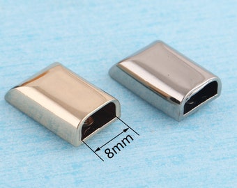 Könnte beinhalten: Zwei Metall-Endkappen für einen Riemen oder eine Schnur. Die Endkappen sind 8 mm lang und haben eine silberne und schwarze Oberfläche.