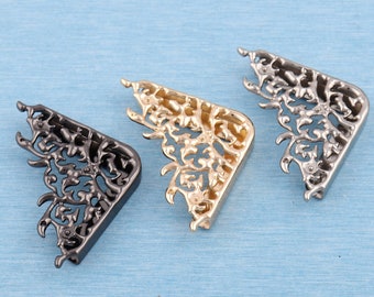 Può includere: Tre staffe d'angolo decorative in oro, argento e nero con un design a filigrana.