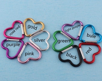 May include: Assortment of eight heart-shaped metal keychains in various colors, including rose red, gold, silver, purple, pink, light purple, green, blue, and black. Each keychain has a spring-loaded gate.