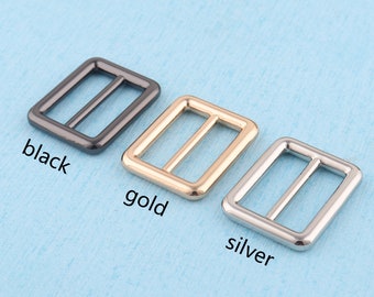 May include: Three metal buckles in black, gold, and silver. The buckles are rectangular with a center bar.