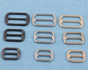 May include: Assortment of metal slider buckles in black, silver, and gold finishes. The buckles are rectangular with two oval openings.