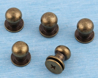 May include: Five antique gold-toned metal knobs with a round top and a flat base. The knobs have a screw-on design.