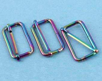 Könnte beinhalten: Drei rechteckige Metall-Gurtversteller mit einer schillernden Regenbogen-Oberfläche. Jede Schiebeschnalle besitzt einen glatten, abgerundeten Rahmen mit einem Mittelsteg und zeigt ein Spektrum aus metallischen Blau-, Grün- und Violetttönen.