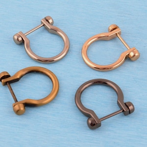 Könnte beinhalten: Vier U-förmige Metallverbinder, die jeweils mit einer geraden Querstange und kleinen abgerundeten Endkappen versehen sind. Das Set enthält ein silberfarbenes, ein roségoldfarbenes, ein mattes bronzefarbenes und ein dunkelgraues Stück.