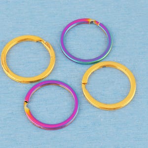 May include: Four circular metal split rings arranged in a cluster. Two of the rings feature a solid gold-tone finish, while the other two rings display a vibrant, iridescent rainbow gradient finish that shifts between shades of purple, blue, and pink.
