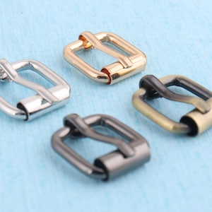 May include: Four metal belt buckles in different finishes: silver, gold, brass, and black. Each buckle has a rectangular shape with a smooth, polished surface.