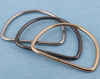 May include: Three metal D-ring bag handles in different finishes: silver, black, and gold. The handles are stacked on top of each other.