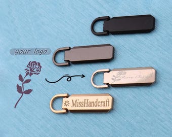 Peut inclure: Quatre tirettes de fermeture éclair rectangulaires en métal avec des extrémités arrondies et des boucles. Les deux du haut sont noir mat et gris foncé. Celles du bas sont en or rose et or, avec des roses gravées et le texte MissHandcraft.