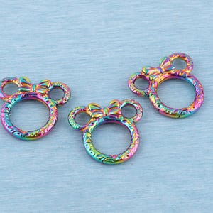 May include: Three circular spring gate rings with a rainbow iridescent finish. Each ring features two small circular ears and a central bow detail at the top, creating a mouse-like silhouette. The metal surface has a textured, engraved pattern.