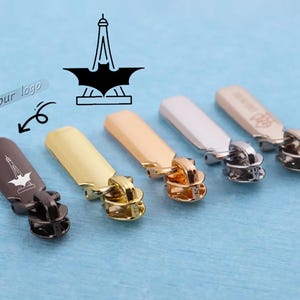May include: Five metal zip pulls in different finishes including matte black, gold, rose gold, silver, and gunmetal. Each pull features a laser-engraved graphic of the Eiffel Tower combined with a bat silhouette. The text your logo is visible.