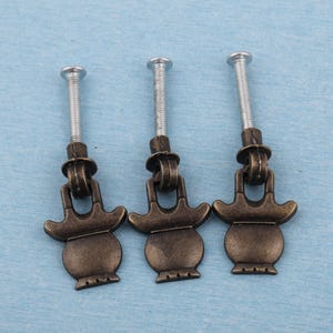 May include: Three antique bronze-colored cabinet pulls with silver screws. Each pull has a decorative, vase-like design with a curved handle and a threaded screw for easy installation. The pulls are set against a light blue background.