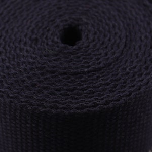 May include: A close-up of a roll of dark blue webbing. The webbing is woven with a textured pattern.