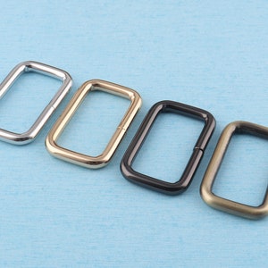 May include: Four metal D-rings in different finishes: silver, gold, black, and bronze. The rings are arranged in a row from left to right.