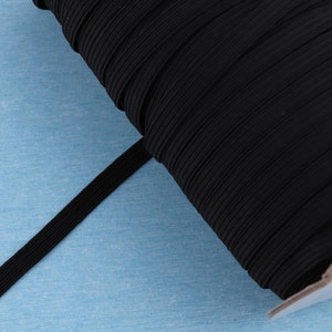 May include: A spool of black elastic band, ideal for sewing and crafting projects. The elastic is tightly wound, showing its ribbed texture and flexibility. The band is a solid black color.