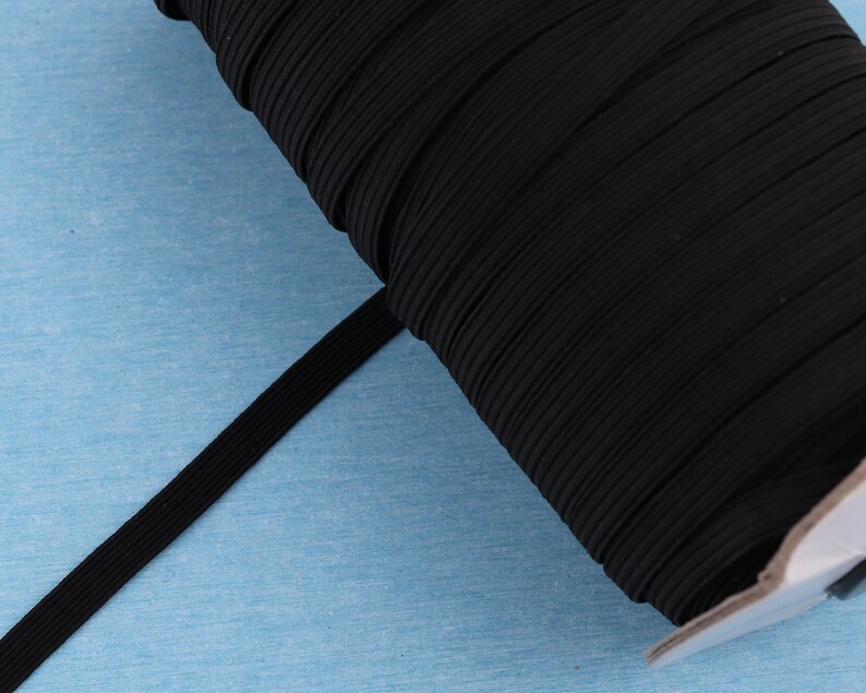 May include: A spool of black elastic band, ideal for sewing and crafting projects. The elastic is tightly wound, showing its ribbed texture and flexibility. The band is a solid black color.
