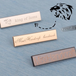 Może przedstawiać: Trzy prostokątne metalowe tabliczki z wygrawerowanym tekstem i grafiką lwa. Górna tabliczka głosi "king of lions", środkowa tabliczka "Miss Handcraft handmade", a dolna tabliczka "Miss Handcraft".