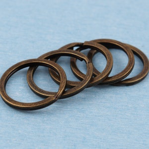 Può includere: Cinque portachiavi in metallo color oro antico, impilati e sovrapposti, su una superficie blu chiaro.