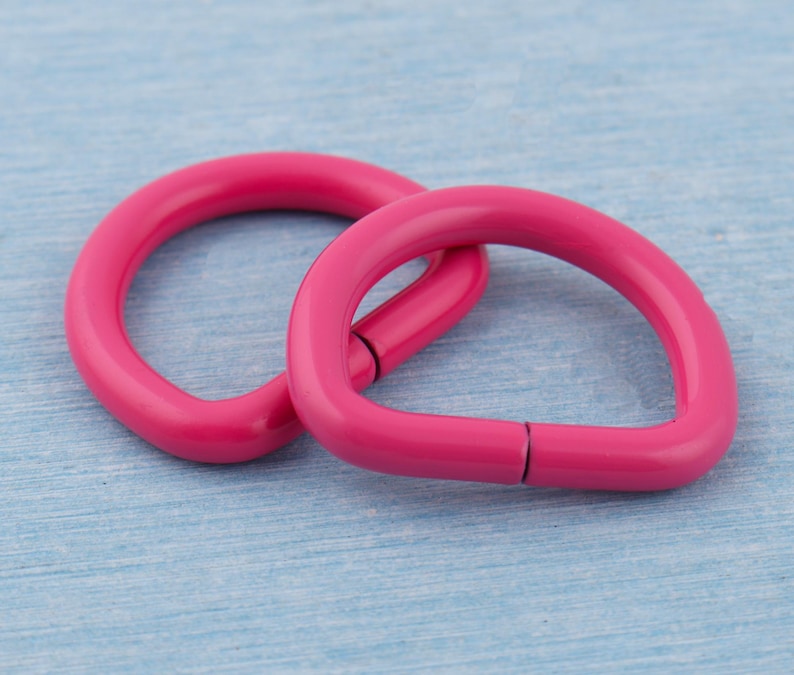 Pu&ograve; includere: Due anelli a D rosa acceso, uno parzialmente sovrapposto all'altro, su uno sfondo azzurro chiaro. Gli anelli a D sono realizzati in un materiale solido e hanno una finitura liscia e lucida. Probabilmente vengono utilizzati per l'artigianato o gli accessori.