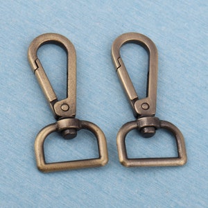 May include: Two antique gold-toned metal swivel clasps with a D-ring. The clasps are closed.