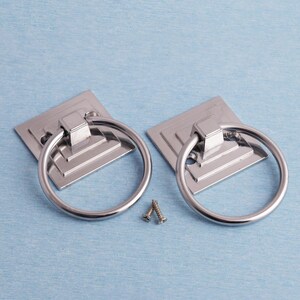 K&ouml;nnte beinhalten: Zwei silberfarbene Schrankgriffe mit quadratischen Grundplatten und runden Griffen. Zwei kleine Schrauben sind ebenfalls zu sehen. Sie liegen auf einem hellblauen Hintergrund. Geeignet f&uuml;r M&ouml;bel.