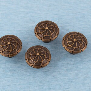 May include: Four bronze cabinet knobs with a floral design. Each knob has a circular shape with a detailed, symmetrical pattern of curved lines radiating from a central point. The knobs are set against a light blue background.