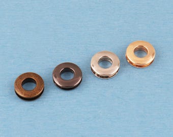 May include: Four circular metal grommets arranged in a diagonal line. The grommets feature distinct finishes including a matte antique bronze, a polished dark gunmetal, a smooth rose gold, and a bright polished gold tone, each with a center hole.