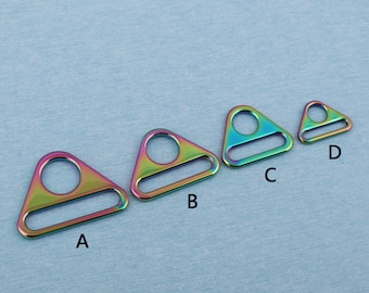 Puede incluir: Cuatro anillos metálicos triangulares iridiscentes con un agujero en el centro y una barra plana en la parte superior. Los anillos están etiquetados como A, B, C y D de izquierda a derecha.